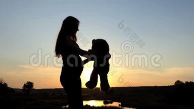 令人惊奇的怀孕女孩在日落时玩大玩具熊。